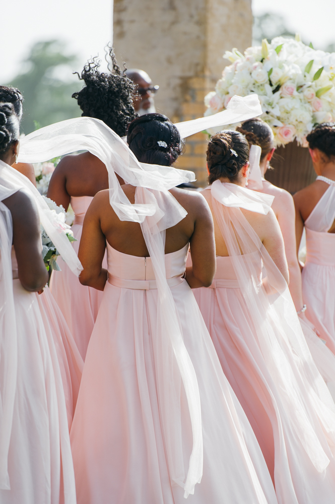 Bridesmaids photographed from behind in their soft pink dresses as the long pieces of fabric from the bow at the back of the neck blow in the wind.

Luxury Texas Wedding Photographer. Timeless Wedding Photography. Wedding in Texas. Destination Wedding Photographer.