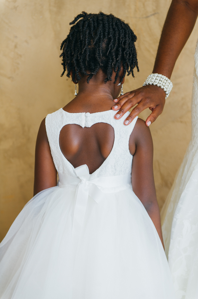 The bride's hand is resting on the shoulder of a flower girl who is facing away from the camera. The bak of her dress has a cutout in the shape of a heart.

Luxury Texas Wedding Photographer. Timeless Wedding Photography. Wedding in Texas. Destination Wedding Photographer.