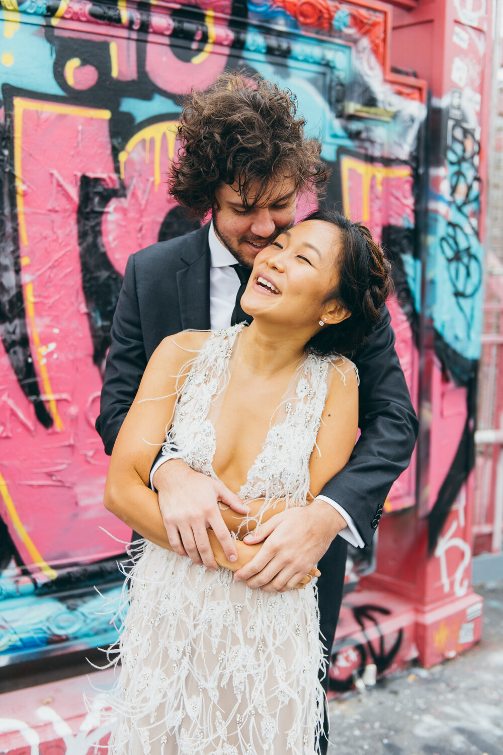 Groom stands behind he bride and he has his arms around her. They are both smiling. A wall of graffiti is behind them on the Williamsburg Bridge.

Central Park Wedding Photography. Williamsburg Bridge Bridal Portraits. Luxury NYC Wedding Photographer. Manhattan Micro Wedding.