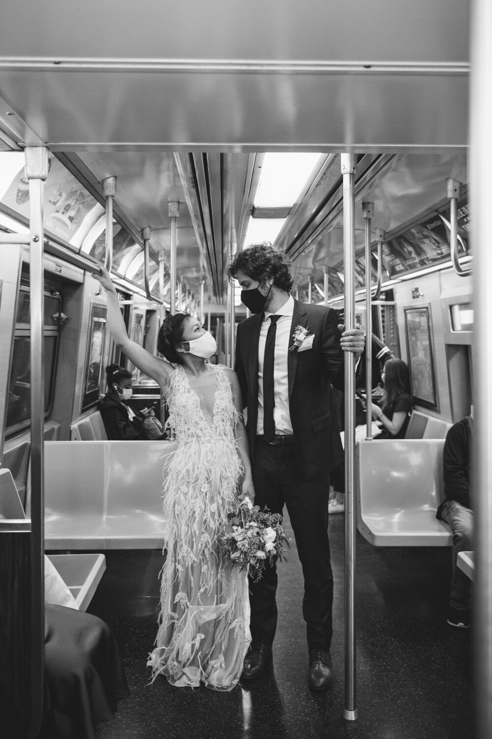 Bride and groom stand in a subway car and hold on to the poles. They are both wearing masks and looking into each other's eyes. 

Central Park Wedding Photography. Williamsburg Bridge Bridal Portraits. Luxury NYC Wedding Photographer. Manhattan Micro Wedding.