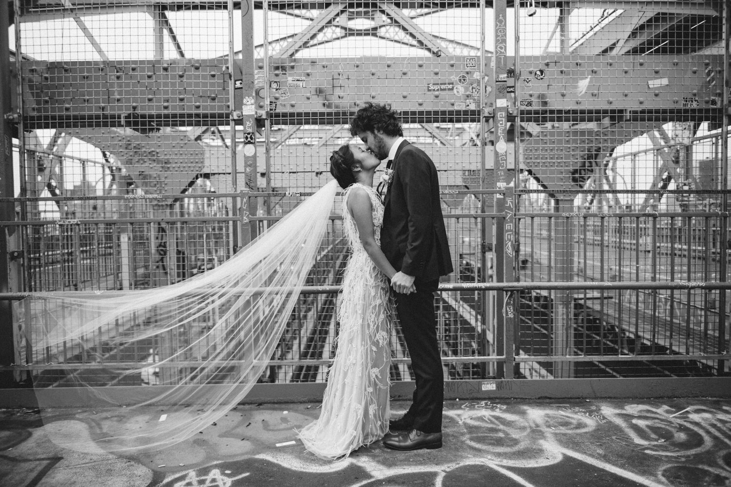 Bride and groom stand facing each other on the Williamsburg Bridge holding hands and they kiss. Her veil is blowing in the wind behind her.

Central Park Wedding Photography. Williamsburg Bridge Bridal Portraits. Luxury NYC Wedding Photographer. Manhattan Micro Wedding.