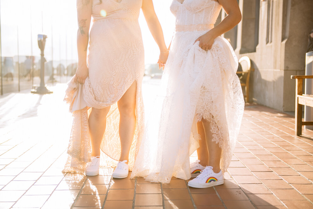 Two brides photographed from the chest down. They are standing outside at Top of the Rock, holding hands and holding up their dress skirts to reveal white sneakers.

Luxury NYC Wedding Photography. Queer Wedding Photography. Inclusive Wedding Photographer. LGBTQ+ Manhattan Wedding.
