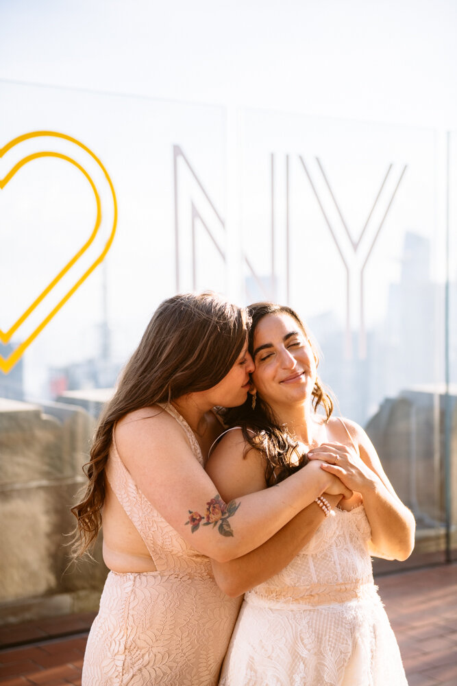 One bride stands behind the other with arms around her and kisses her on the cheek. They are smiling at the Top of the Rock.

Luxury NYC Wedding Photography. Queer Wedding Photography. Inclusive Wedding Photographer. LGBTQ+ Manhattan Wedding.