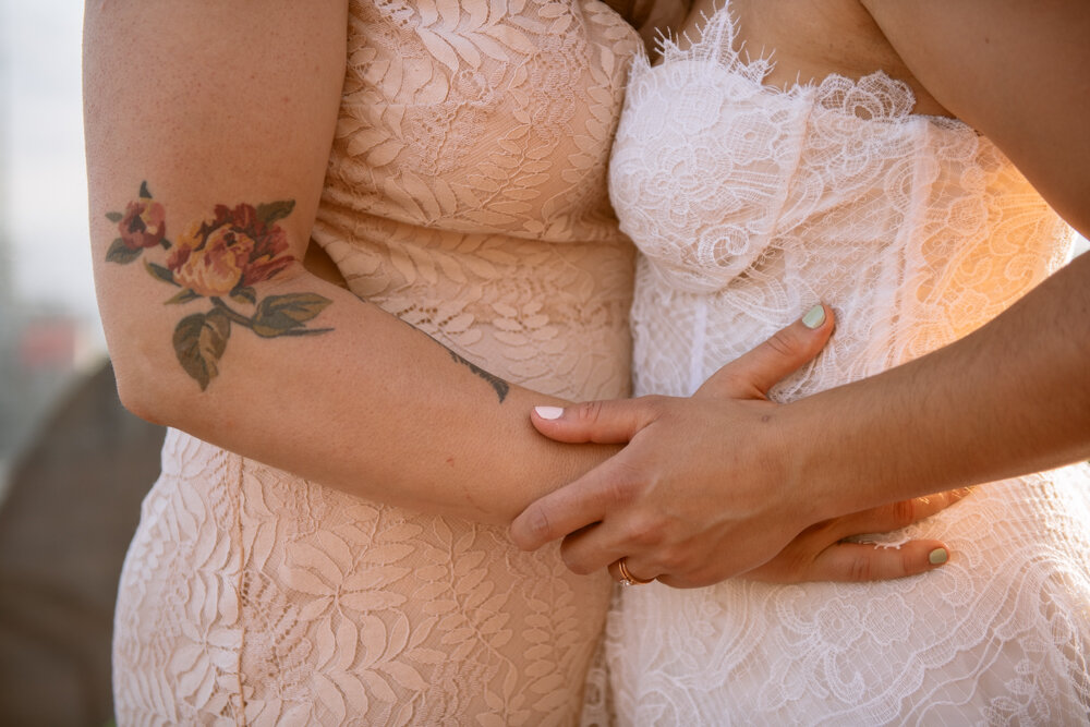 Closeup image of the two brides holding hands on each other's waists. One bride has a flower tattooed on her elbow.

Luxury NYC Wedding Photography. Queer Wedding Photography. Inclusive Wedding Photographer. LGBTQ+ Manhattan Wedding.