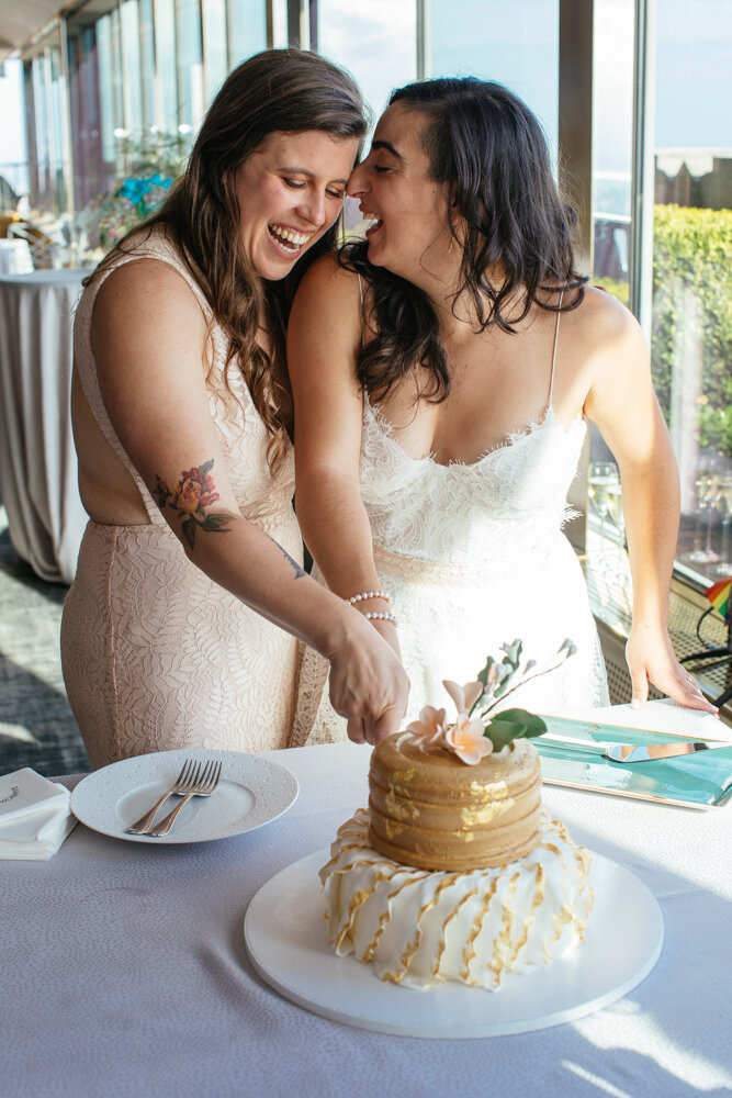 Brides hold a knife together and cut a slice of wedding cake. One bride is smiling looking down at the cake and the other bride is smiling and looking at her bride.

Luxury NYC Wedding Photography. Queer Wedding Photography. Inclusive Wedding Photographer. LGBTQ+ Manhattan Wedding.