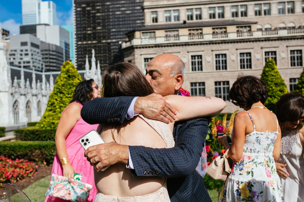 One bride hugs a man who kisses her on the cheek. Wedding guests are seen behind them at Top of the Rock.

Luxury NYC Wedding Photography. Queer Wedding Photography. Inclusive Wedding Photographer. LGBTQ+ Manhattan Wedding.