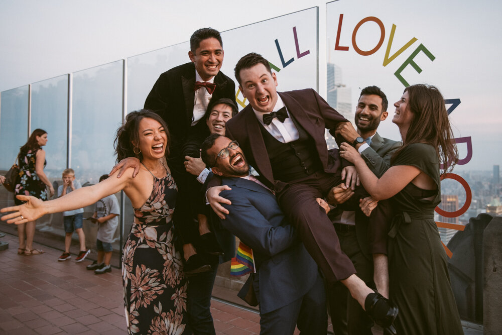 Grooms are held in the air by wedding guests as they all smile and laugh.

Luxury NYC Wedding Photography. Queer Wedding Photography. Inclusive Wedding Photographer. LGBTQ+ Manhattan Wedding.