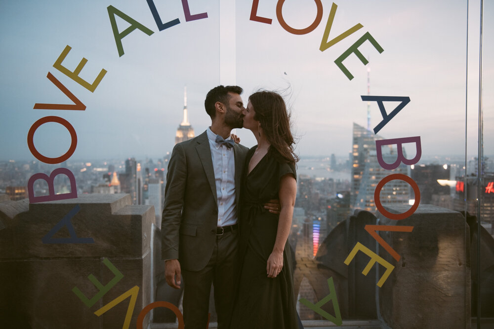 Two wedding guests kiss at Top of the Rock in front of the "LOVE ABOVE ALL" sign.

Luxury NYC Wedding Photography. Queer Wedding Photography. Inclusive Wedding Photographer. LGBTQ+ Manhattan Wedding.