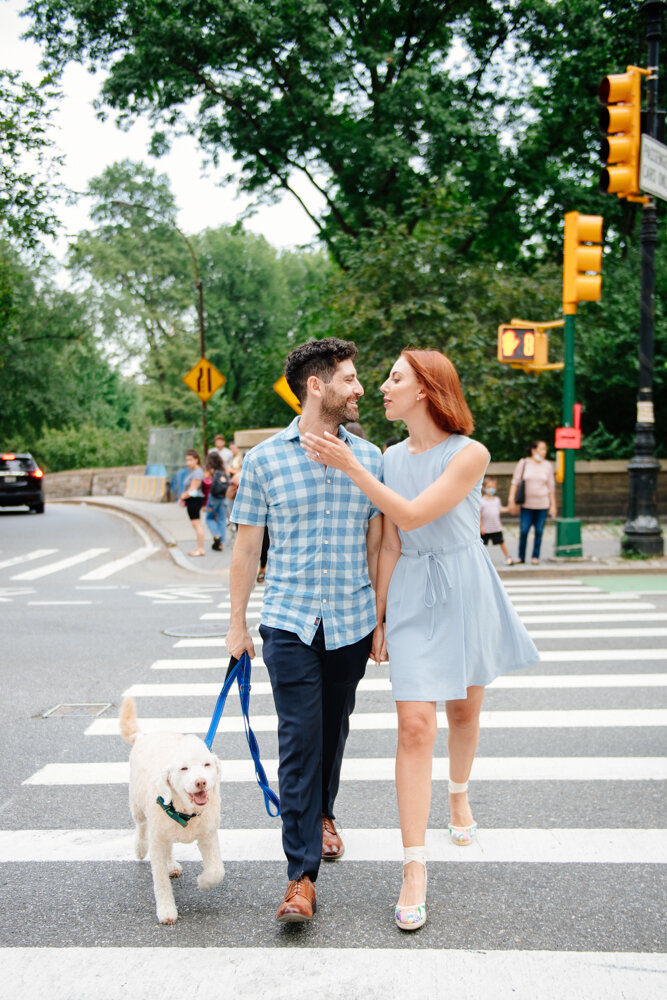 Man holds the leash to a fluffy white dog walking next to him as he looks over to the woman walking on the other side of him and she leans in to kiss him.

Central Park Engagement Portraits. Manhattan Engagement Photography. NYC Engagement Photographer.