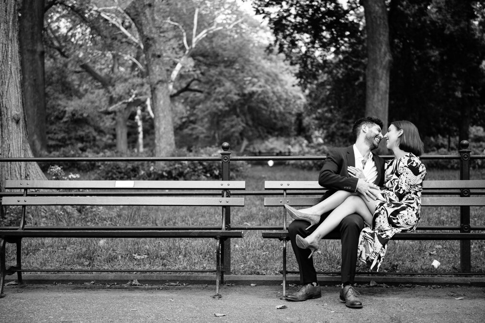 Man and woman are sitting on a bench in Central Park in Manhattan. She is facing him on the bench and has her legs on his lap. They are touching noses and smiling.

Central Park Engagement Portraits. Manhattan Engagement Photography. NYC Engagement Photographer.