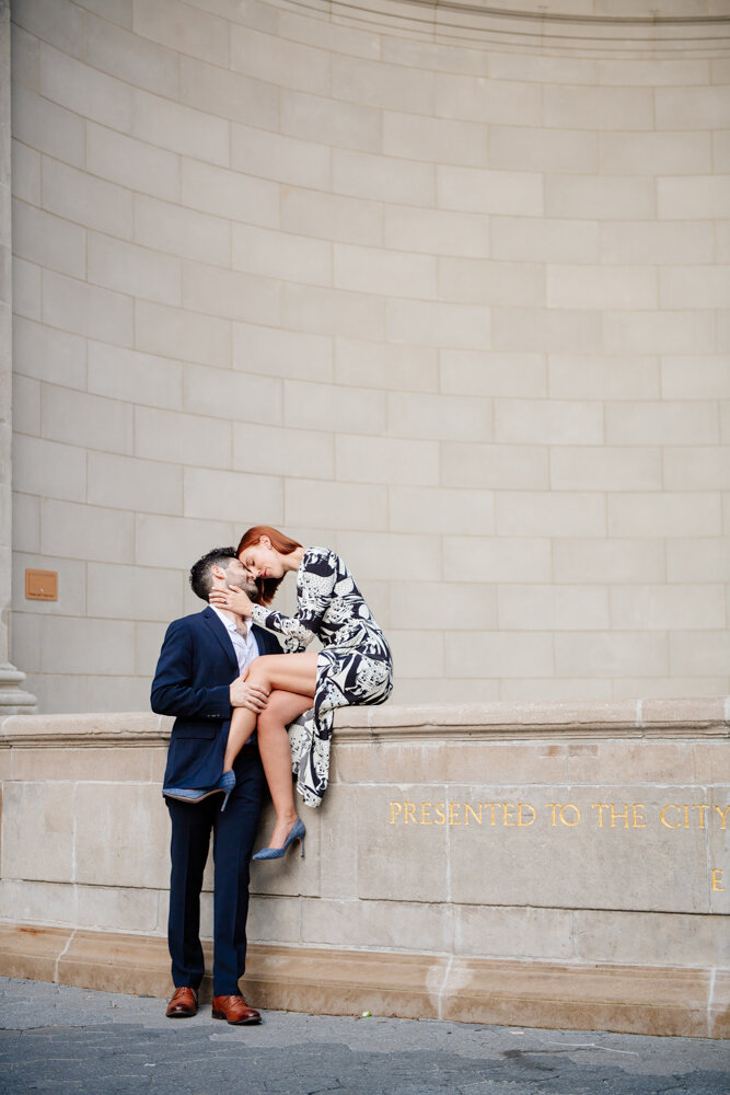 Man is standing on the ground next to the bandshell in Central Park. Woman is sitting on the bandshell stage and he has his hand on her crossed leg. They are touching foreheads and smiling.

Central Park Engagement Portraits. Manhattan Engagement Photography. NYC Engagement Photographer.