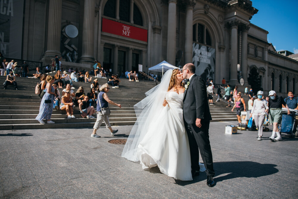 Bride and groom kiss out front of the Metropolitan Museum of Art in Manhattan. Pedestrians and people sitting on the steps of the Met look on at the bride and groom.

Luxury Local Wedding NYC. Wedding in Manhattan. New York City Wedding Photographer. Manhattan Luxury Wedding Photography. Museum of the City of New York Weddings.