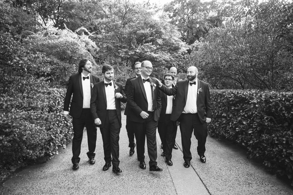 Groom and his groomsmen all walk together and look at each other, smile, and a groomsman has a hand on the groom's shoulder.

Luxury Local Wedding NYC. Wedding in Manhattan. New York City Wedding Photographer. Manhattan Luxury Wedding Photography. Museum of the City of New York Weddings.