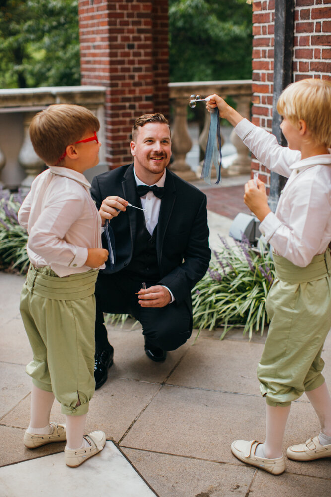The two ring bearers are holding out bubble wands to show one of the wedding guests outside the Museum of the City of New York.

Luxury Local Wedding NYC. Wedding in Manhattan. New York City Wedding Photographer. Manhattan Luxury Wedding Photography. Museum of the City of New York Weddings.