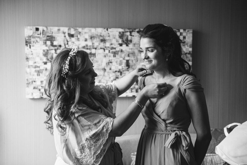 Bride is in a robe and white headband reaching over to a bridesmaid and adjusting her necklace. She smiles at the bride.

Luxury Local Wedding NYC. Wedding in Manhattan. New York City Wedding Photographer. Manhattan Luxury Wedding Photography. Museum of the City of New York Weddings.