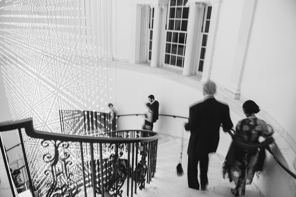 Wedding guests walk down a spiral staircase inside the Museum of the City of New York. There is a motion blur.

Luxury Local Wedding NYC. Wedding in Manhattan. New York City Wedding Photographer. Manhattan Luxury Wedding Photography. Museum of the City of New York Weddings.