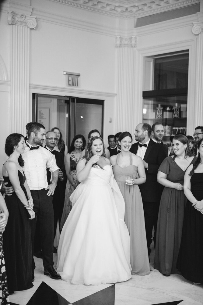 Bride is standing surrounded by her wedding guests and he groom and she has a big smile on her face.

Luxury Local Wedding NYC. Wedding in Manhattan. New York City Wedding Photographer. Manhattan Luxury Wedding Photography. Museum of the City of New York Weddings.