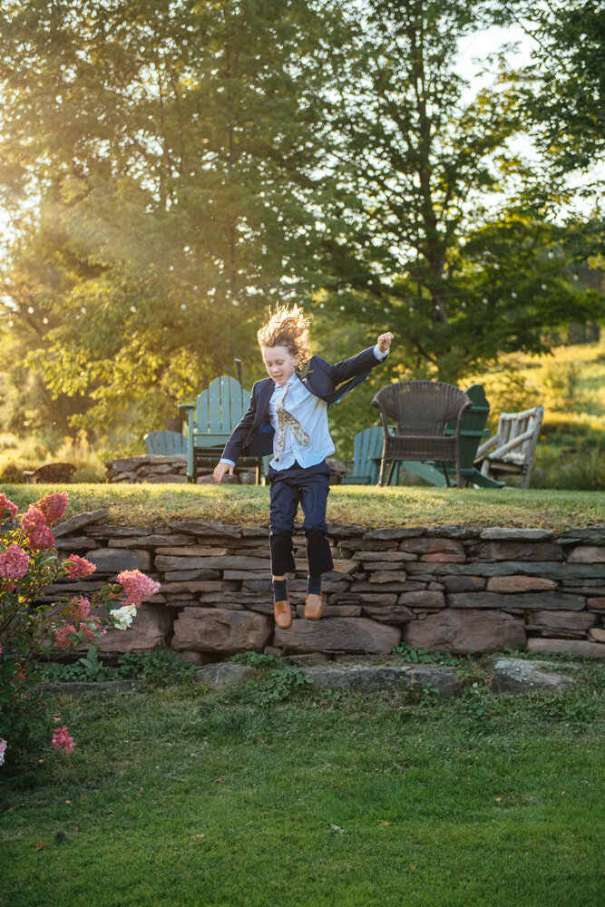 A young child in a suit jumps off of a short stone wall onto a grassy area.

Upstate New York Wedding Photographer. Upstate NY Wedding Photography. Luxury Local Wedding Upstate NY.