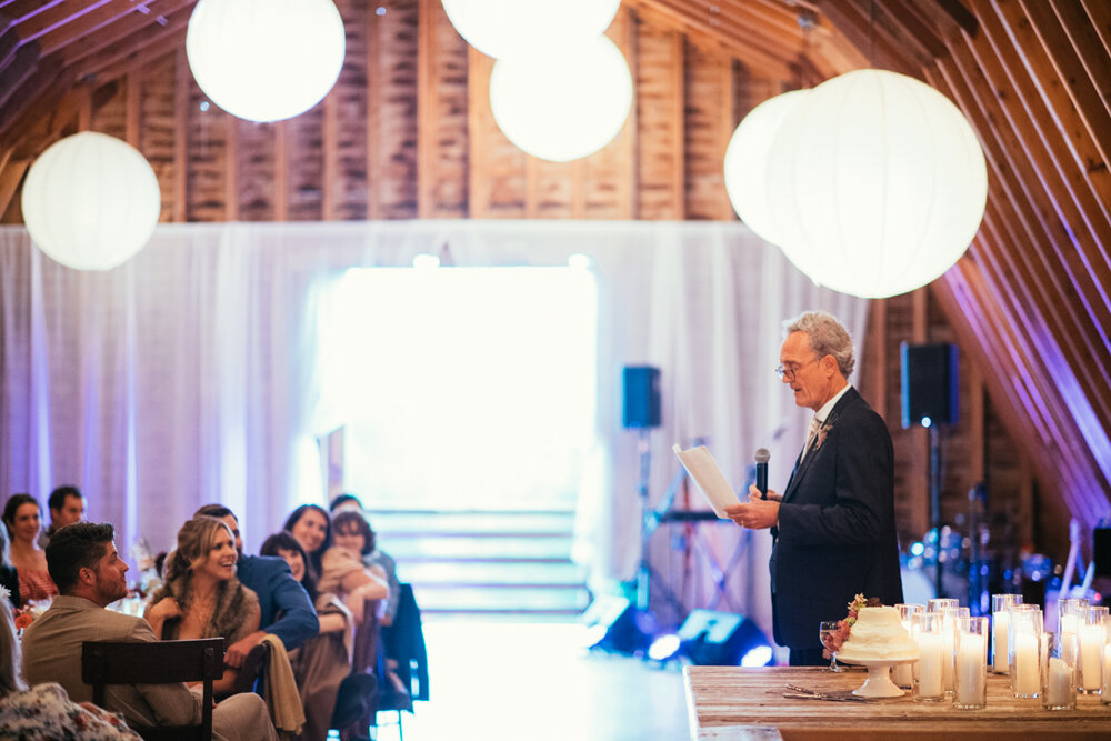 A man stands in the barn and gives a speech as seated wedding guests look on.

Upstate New York Wedding Photographer. Upstate NY Wedding Photography. Luxury Local Wedding Upstate NY.