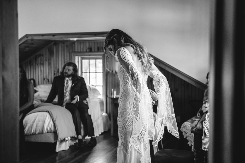 Bride wears a jeweled wedding dress with long flared sleeves and reached behind her to zip up the dress.

Upstate New York Wedding Photographer. Upstate NY Wedding Photography. Luxury Local Wedding Upstate NY.