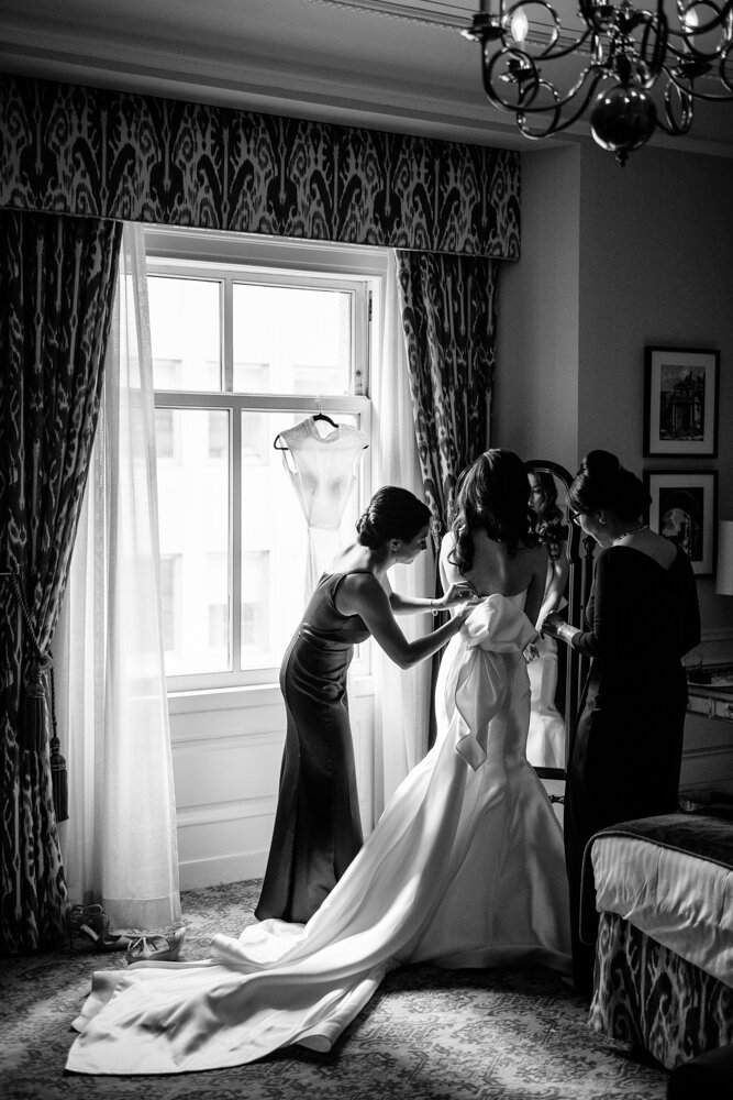 Bride is in her wedding dress and standing in front of a mirror as two women help adjust the bow at the back of her dress. The train of her dress trails across the room.

University Club Wedding Photographer. Manhattan Luxury Wedding Photographer. Manhattan Bridal Portraits. Luxury Local Wedding NYC. 