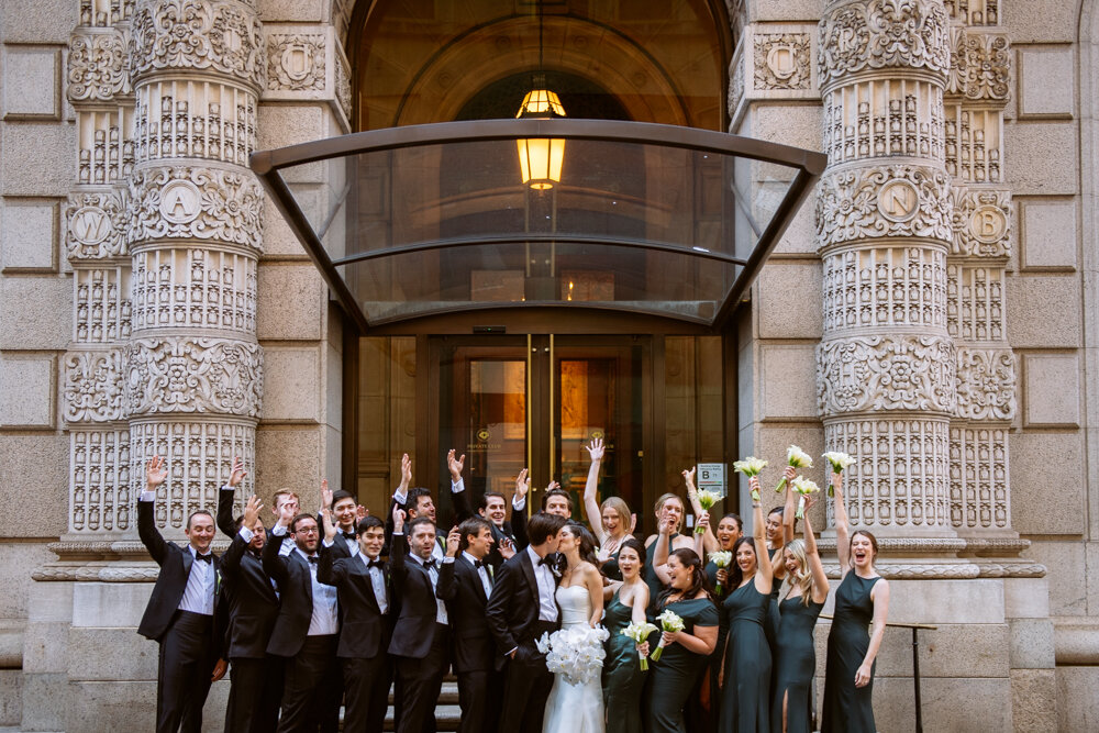 Bride and groom kiss outside the University Club in New York City as their entire bridal party stands around them and cheers with arms in the air.

University Club Wedding Photographer. Manhattan Luxury Wedding Photographer. Manhattan Bridal Portraits. Luxury Local Wedding NYC. 