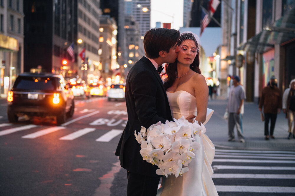 Groom kisses the bride on the cheek on a New York City sidewalk. Cars, buildings, and pedestrians are visible in the background.

University Club Wedding Photographer. Manhattan Luxury Wedding Photographer. Manhattan Bridal Portraits. Luxury Local Wedding NYC. 