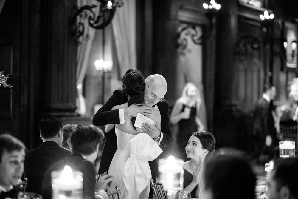 Man hugs the bride as seated wedding guests look on with smiles.

University Club Wedding Photographer. Manhattan Luxury Wedding Photographer. Manhattan Bridal Portraits. Luxury Local Wedding NYC. 