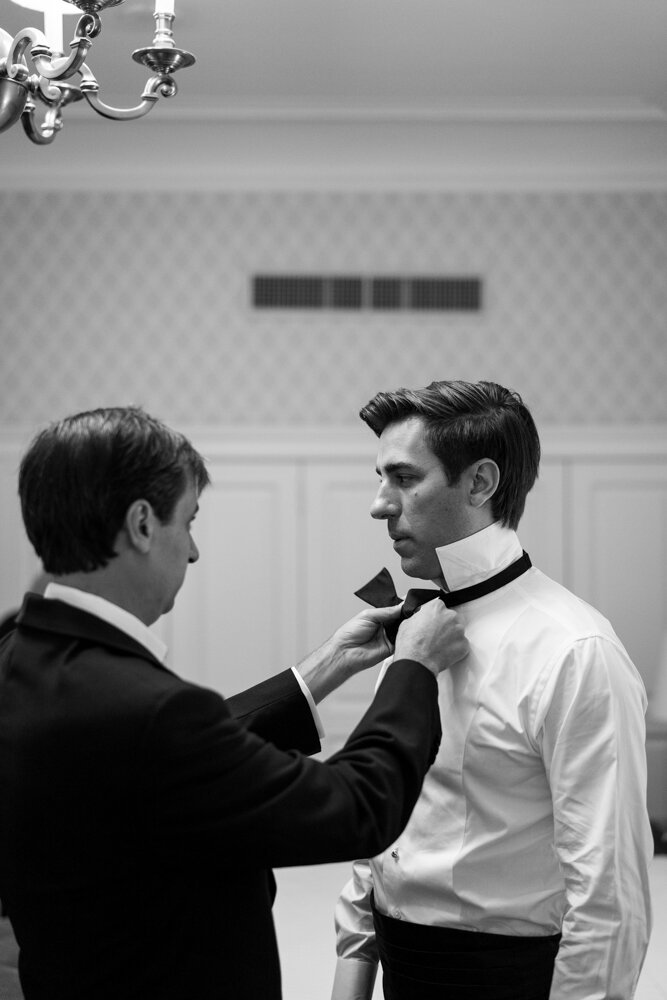 A man ties the groom's bowtie.

University Club Wedding Photographer. Manhattan Luxury Wedding Photographer. Manhattan Groom Portraits. Luxury Local Wedding NYC. 