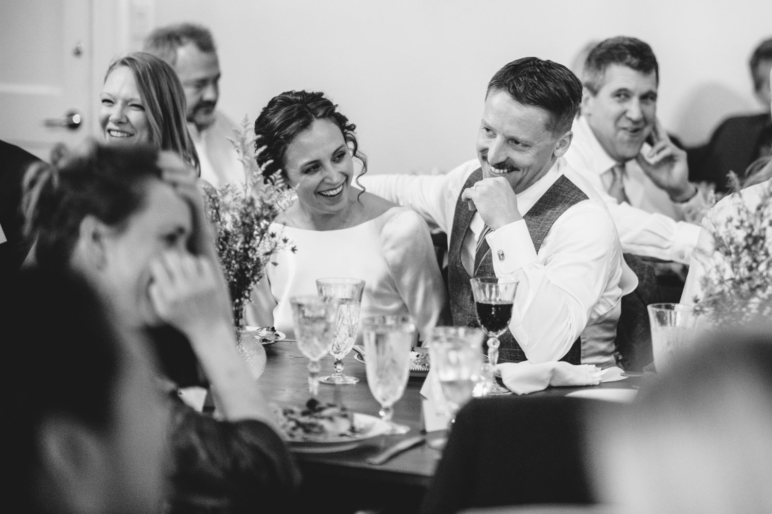 Groom has his arm around the bride as they both laugh and smile, seated among smiling wedding guests.

Upstate New York Wedding Photography. Cold Spring NY Wedding Photography. Luxury Local Wedding Photographer. Destination Wedding Photographer.