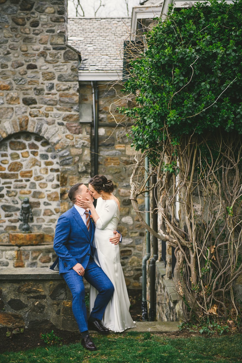 Groom sits on a short stone wall and kisses the bride who is standing next to him.

Upstate New York Wedding Photography. Cold Spring NY Wedding Photography. Luxury Local Wedding Photographer. Destination Wedding Photographer.