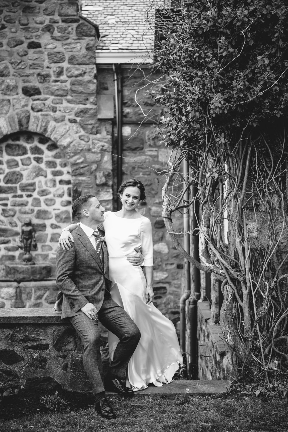 Groom sits on a stone wall and looks at his bride who is standing next to him. Their arms are around each other and she is smiling at the camera.

Upstate New York Wedding Photography. Cold Spring NY Wedding Photography. Luxury Local Wedding Photographer. Destination Wedding Photographer.