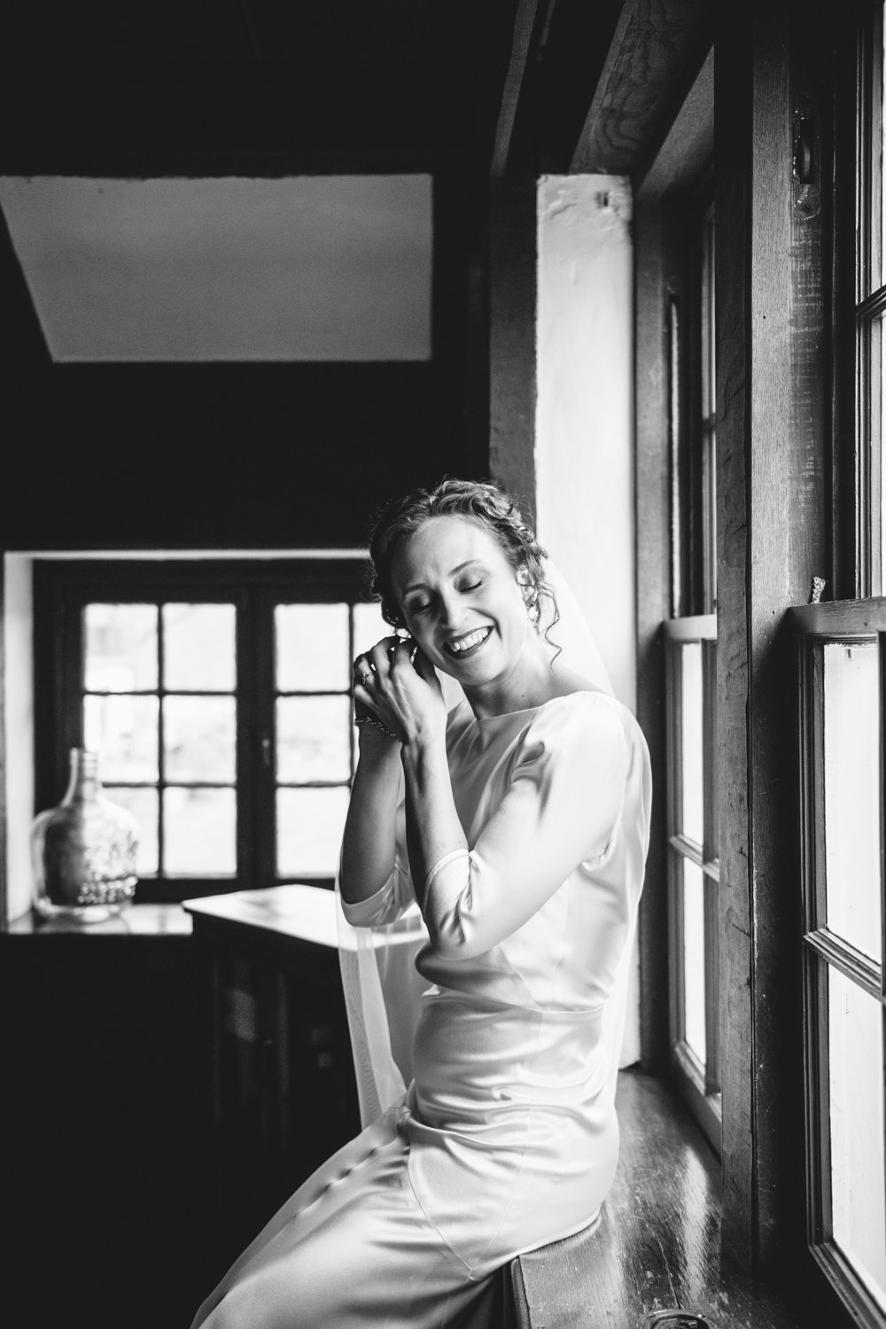 Bride sits on the window sill in her wedding dress and smiles as she adjust her earring.

Upstate New York Wedding Photography. Cold Spring NY Wedding Photography. Luxury Local Wedding Photographer. Destination Wedding Photographer.