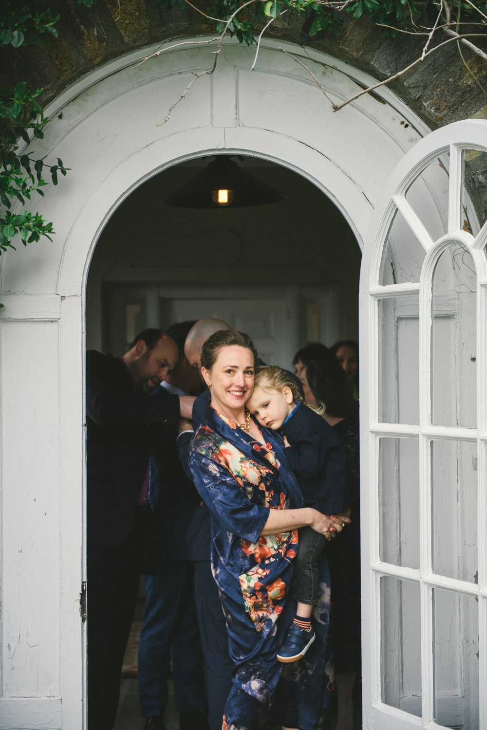 Wedding guest stands in a doorway holding a young boy on her hip and smiles at the camera. Wedding guests are standing behind her.

Upstate New York Wedding Photography. Cold Spring NY Wedding Photography. Luxury Local Wedding Photographer. Destination Wedding Photographer.