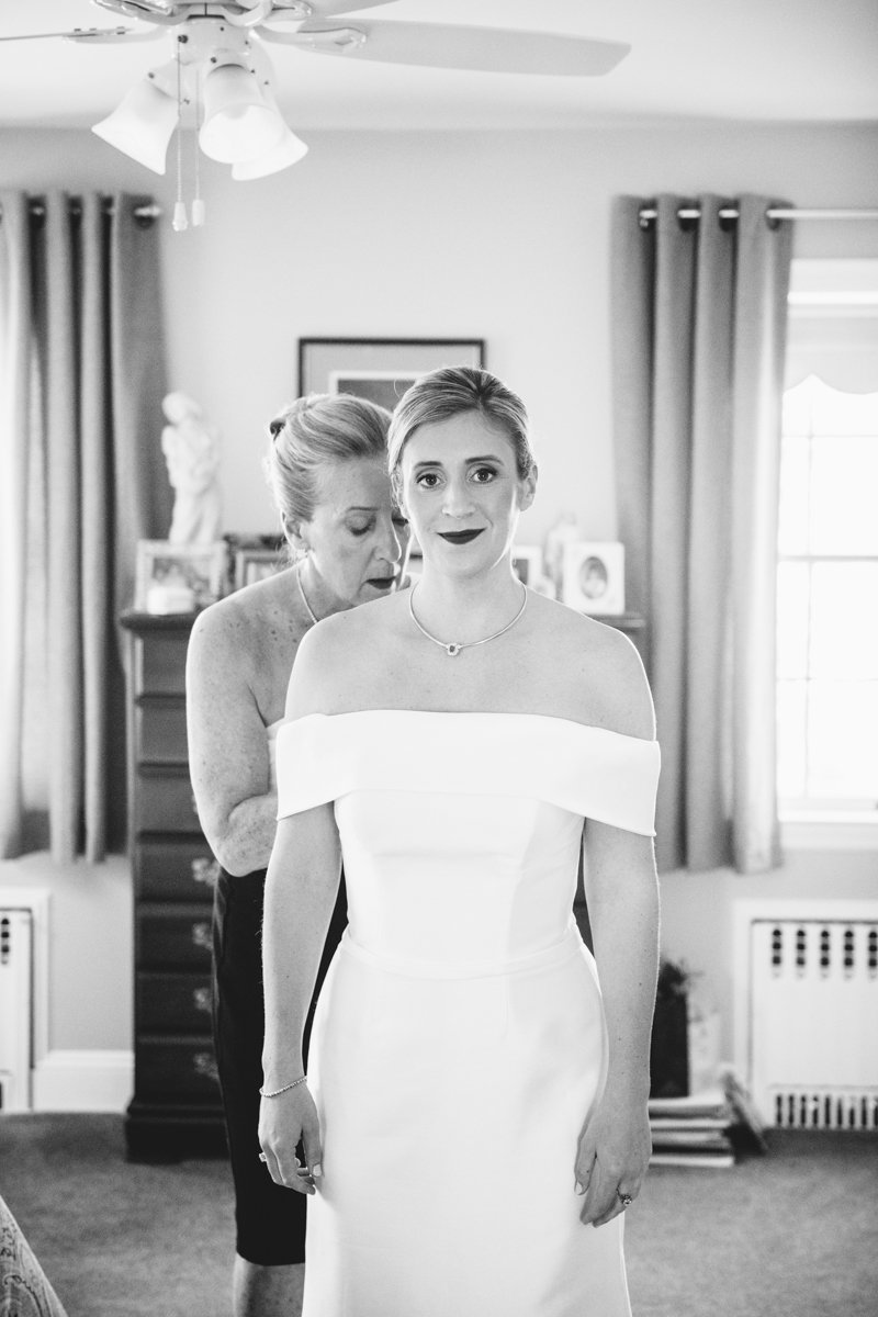 Bride smiles straight on at the camera as her mother helps her zip up her off-the-shoulder wedding dress from behind.

New York Wedding Photography. Long Island Wedding Photography. Luxury Local Wedding Photographer. Destination Wedding Photographer.