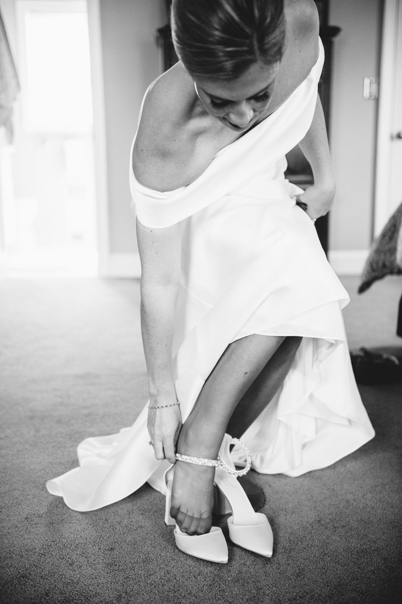 Bride leans over in her off-the-shoulder wedding dress and reaches down to put on her heels.

New York Wedding Photography. Long Island Wedding Photography. Luxury Local Wedding Photographer. Destination Wedding Photographer.