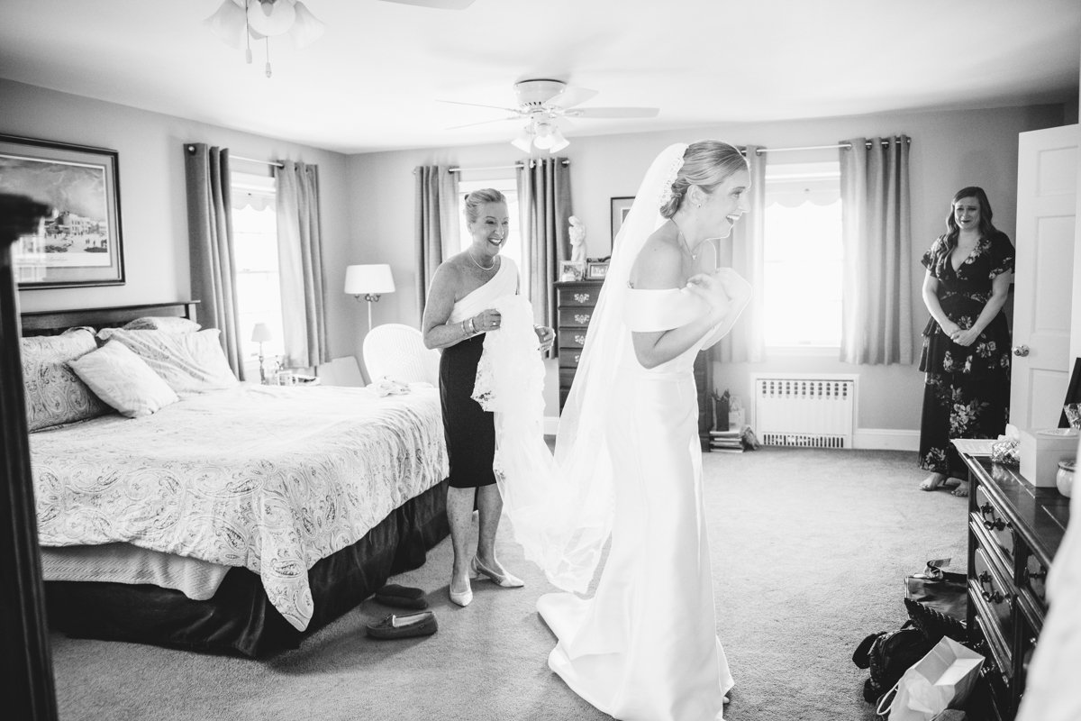 Bride smiles as she looks at herself in the mirror. Her mother is behind her holding the end of her veil and smiling at her daughter.

New York Wedding Photography. Long Island Wedding Photography. Luxury Local Wedding Photographer. Destination Wedding Photographer.