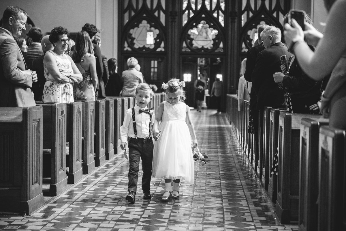 A young girl and boy walk down the aisle of the church as wedding guests look on with smiles.

New York Wedding Photography. Long Island Wedding Photography. Luxury Local Wedding Photographer. Destination Wedding Photographer.