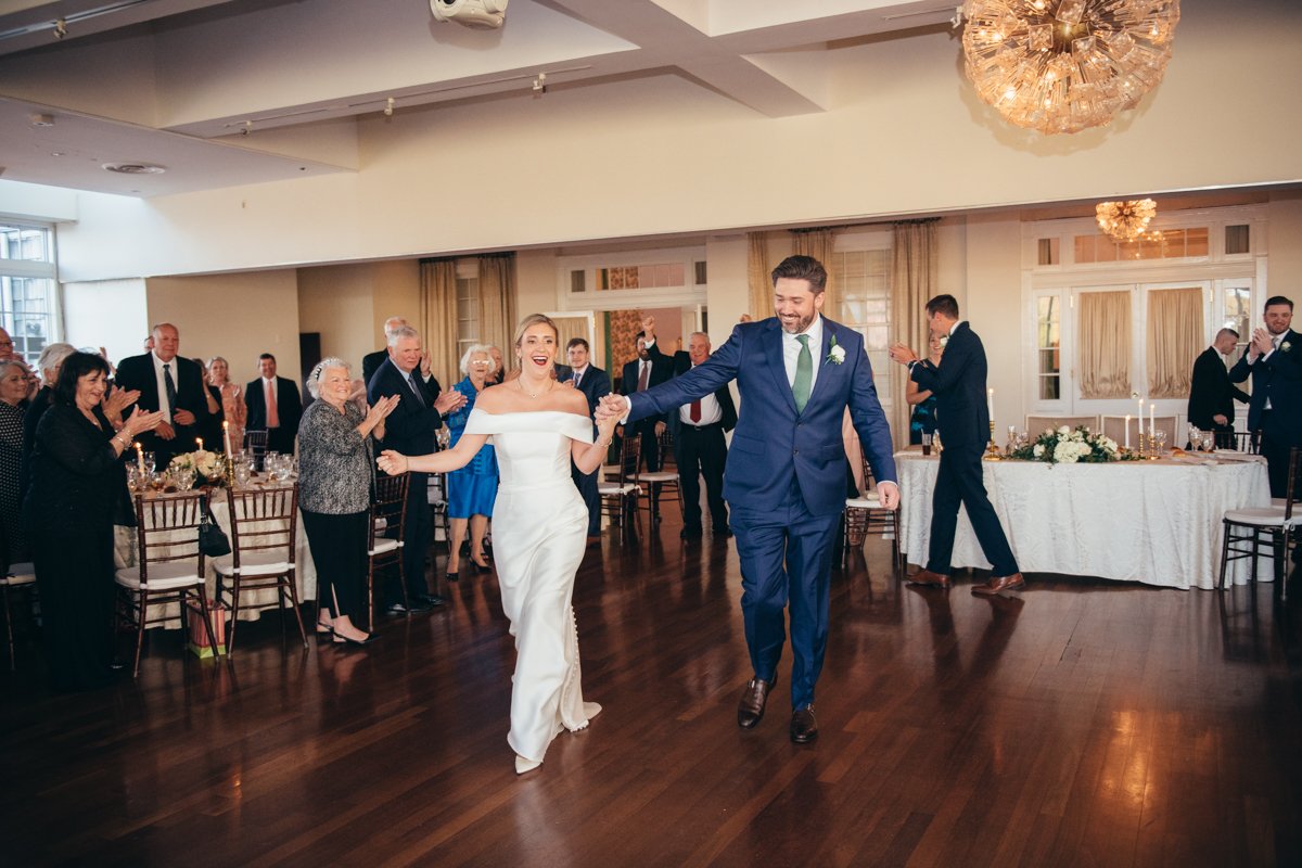 Bride and groom hold hands as they walk onto the dance floor with a smile as wedding guests around them clap.

New York Wedding Photography. Long Island Wedding Photography. Luxury Local Wedding Photographer. Destination Wedding Photographer.