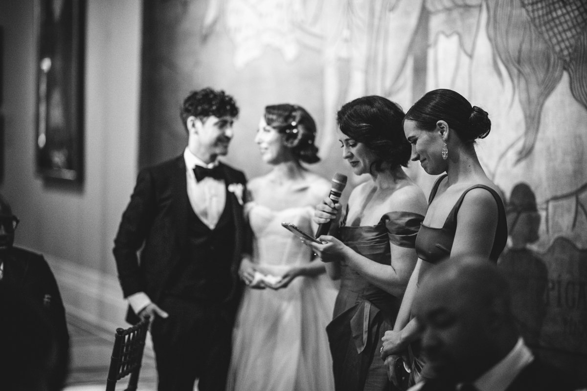 Bride and groom stand in the background as two bridesmaids give a speech standing next to them.

Manhattan Wedding Photographer. New York Wedding Photographer. New York Historical Society Wedding. NY Historical Society Weddings.