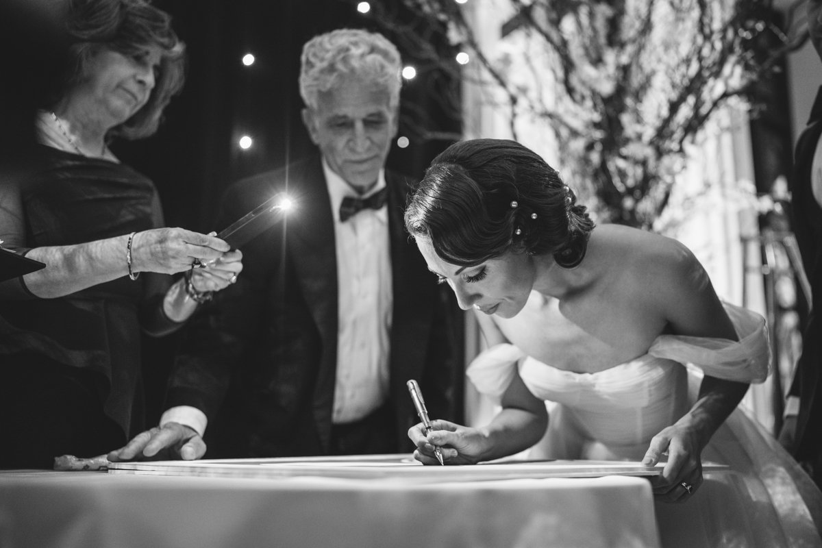 Bride leans over a table with a pen in her hand as the groom's parents stand beside her.

Manhattan Wedding Photographer. New York Wedding Photographer. New York Historical Society Wedding. NY Historical Society Weddings.