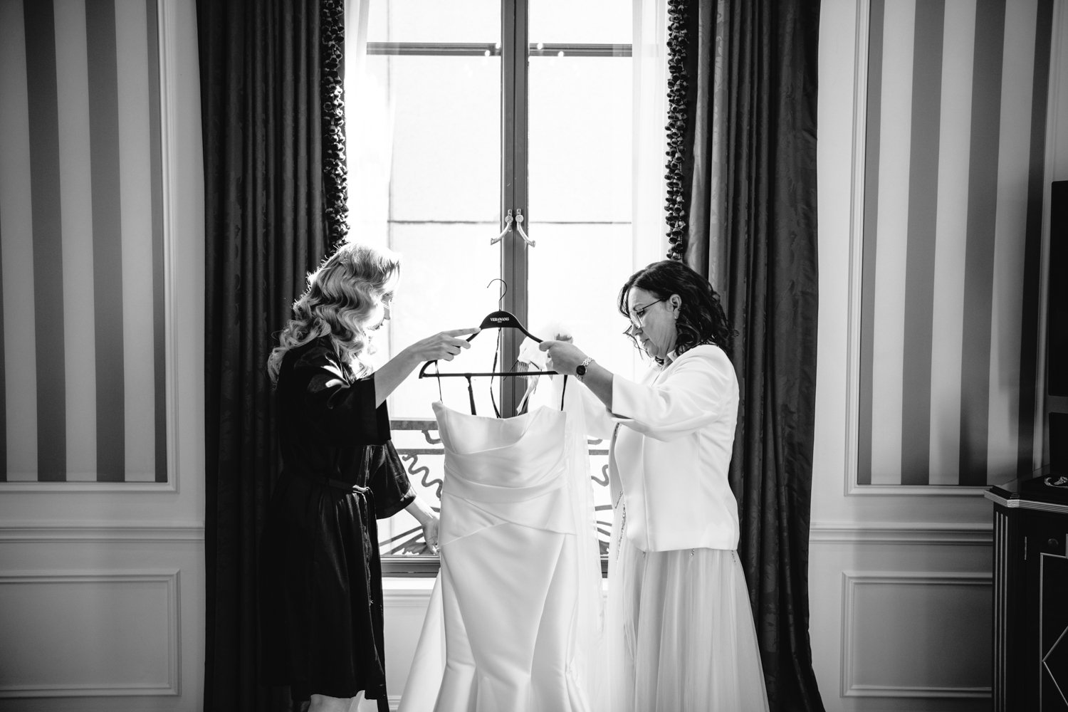 Bride and her mother are holding up the bride's wedding dress against a window.

Manhattan Luxury Wedding. New York Luxury Wedding Photographer. Wedding in Manhattan. NYC Luxury Wedding.
