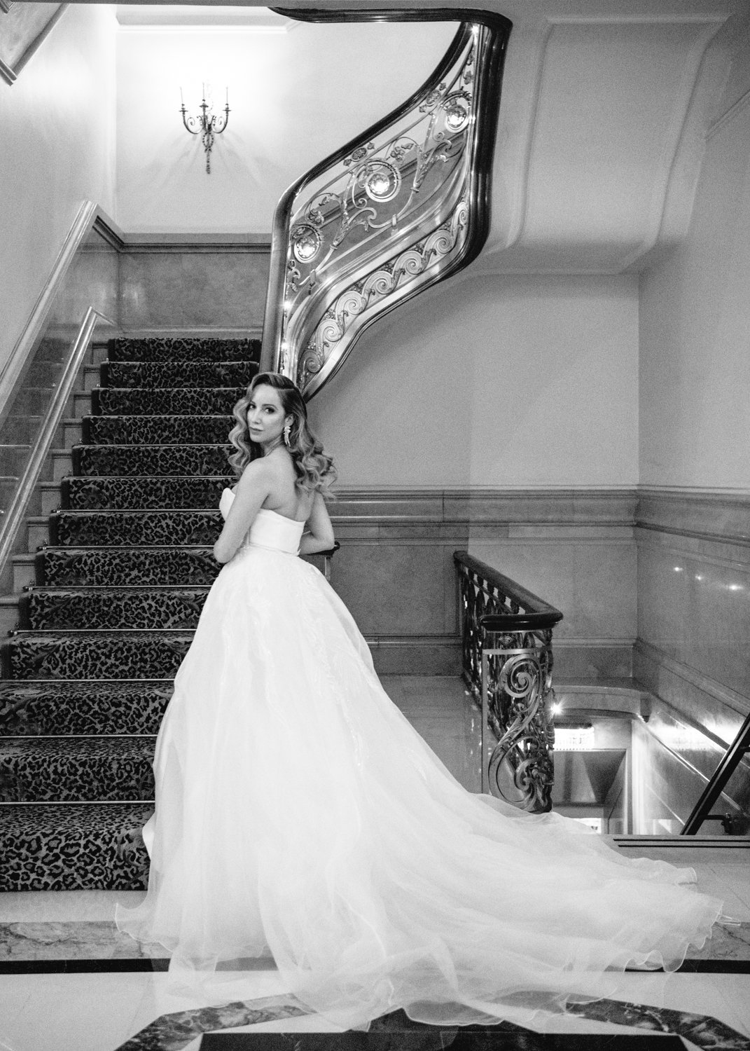 Bride stands at the bottom of a grand staircase in the St. Regis in Manhattan. Her train is flowing behind her.

Manhattan Luxury Wedding. New York Luxury Wedding Photographer. Wedding in Manhattan. NYC Luxury Wedding.