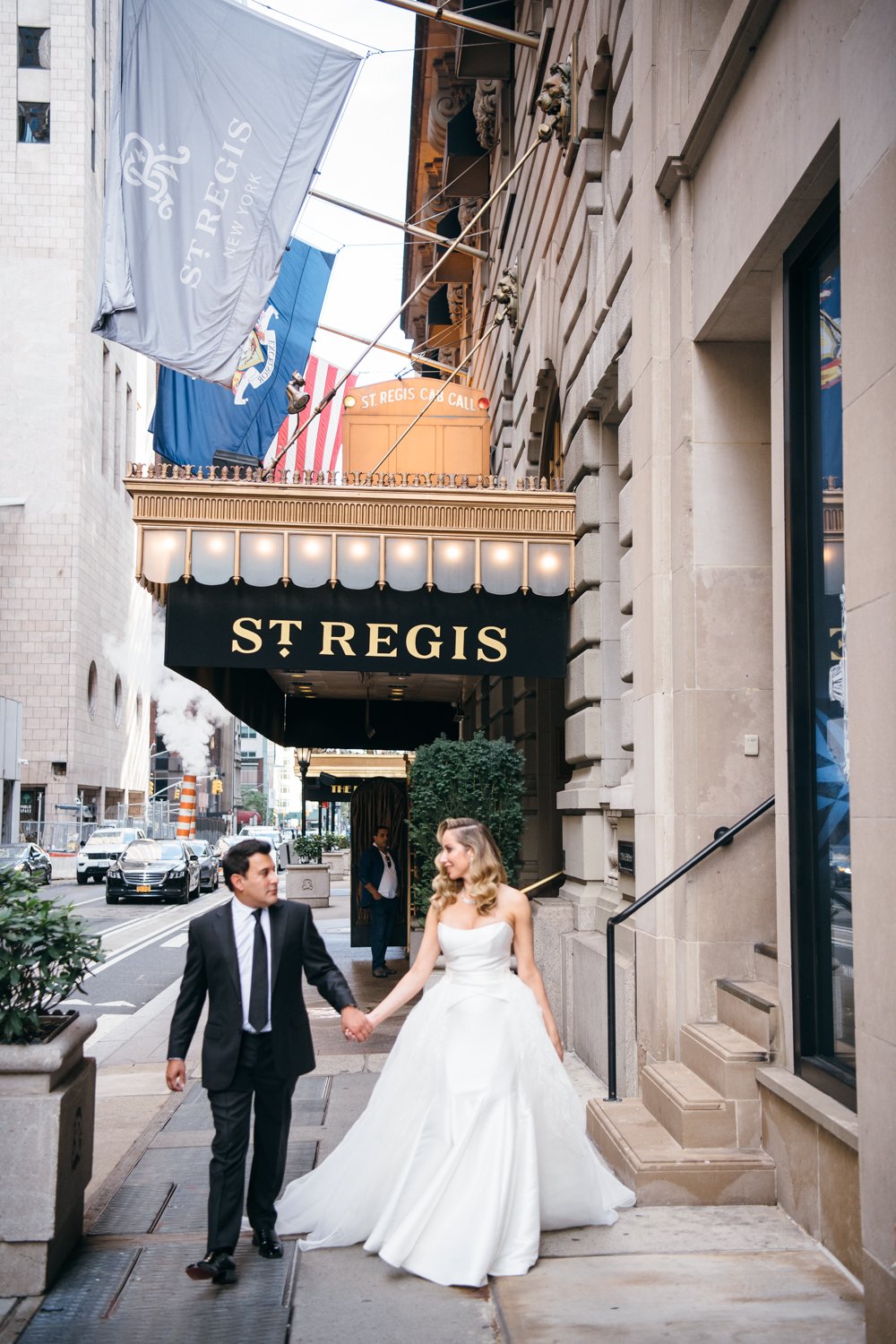 Bride and groom stand side by side holding hands outside the St. Regis in Manhattan. The "St. Regis" awning and "St. Regis" flag are above them.

Manhattan Luxury Wedding. New York Luxury Wedding Photographer. Wedding in Manhattan. NYC Luxury Wedding. Manhattan Bridal Portraits.