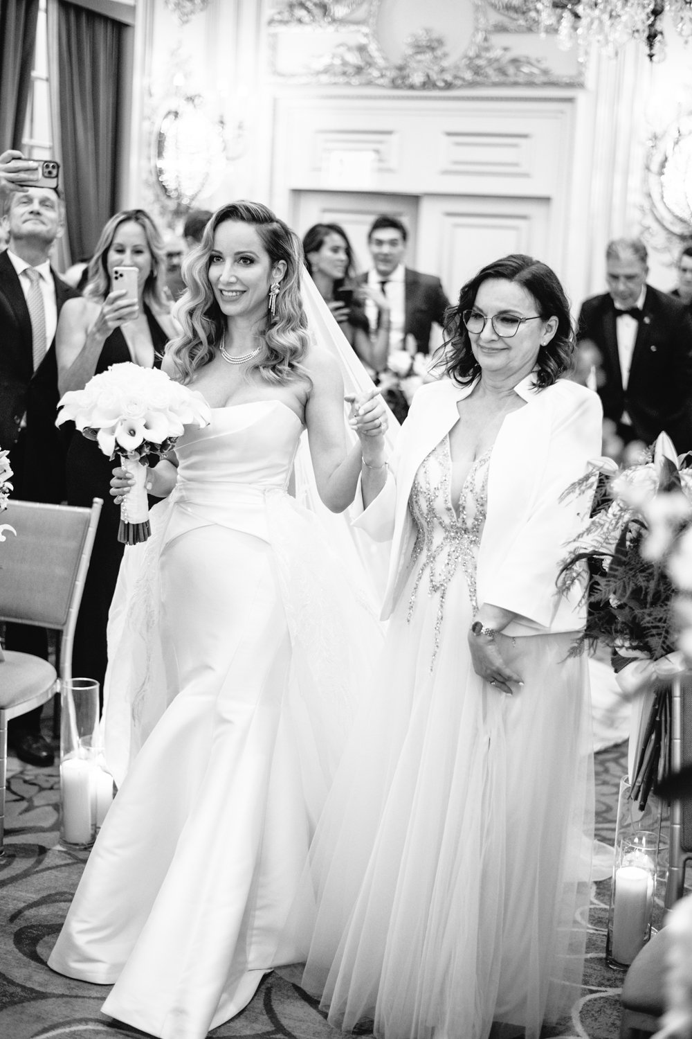 Bride and her mother walk down the aisle smiling and holding hands. The wedding guests are standing and smiling.

Manhattan Luxury Wedding. New York Luxury Wedding Photographer. Wedding in Manhattan. NYC Luxury Wedding.