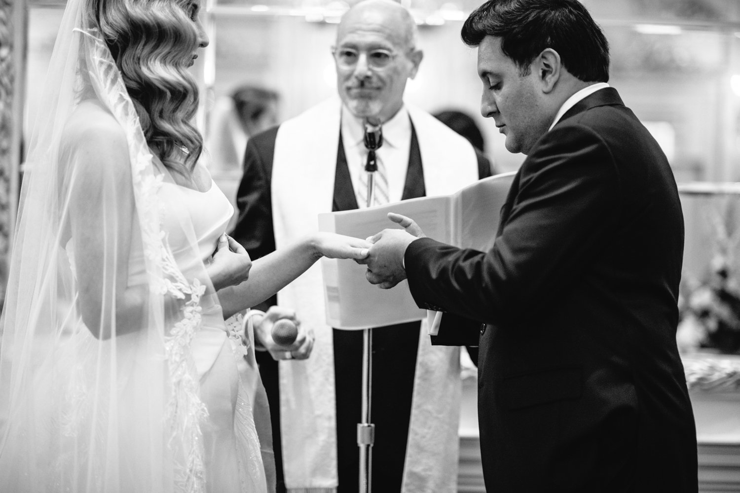 Groom holds the bride's hand at the altar and places a wedding ring on her finger. The wedding officiant stands behind them.

Manhattan Luxury Wedding. New York Luxury Wedding Photographer. Wedding in Manhattan. NYC Luxury Wedding.