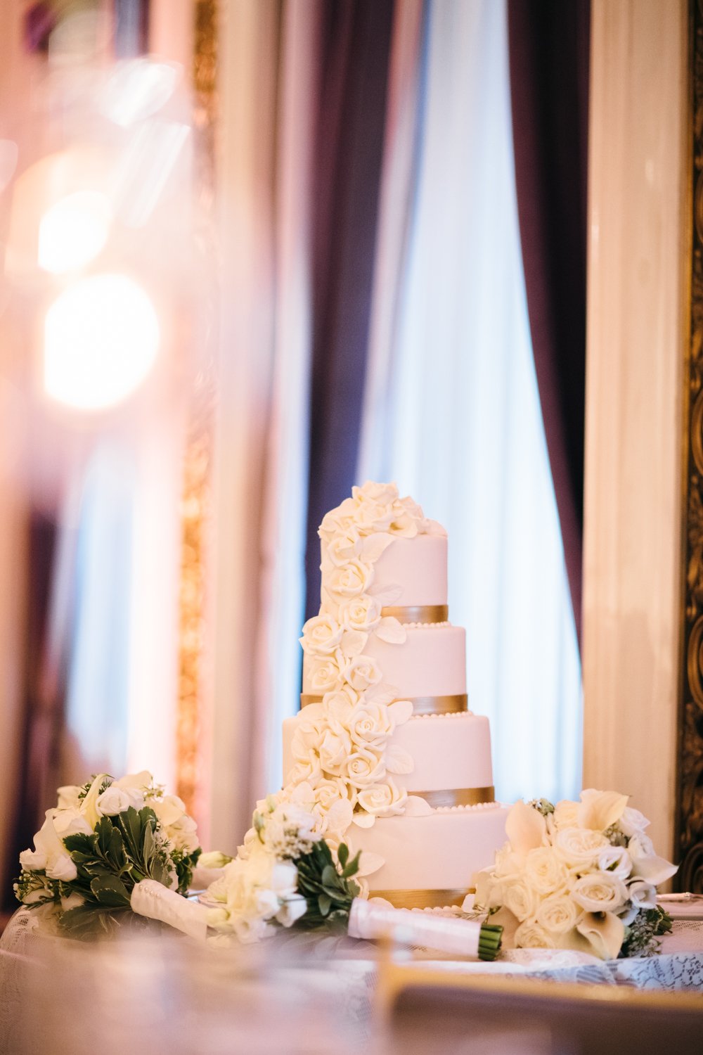 A four-tiered white wedding cake with floral designs sits on a table with white bouquets surrounding it.

Manhattan Luxury Wedding. New York Luxury Wedding Photographer. Wedding in Manhattan. NYC Luxury Wedding.