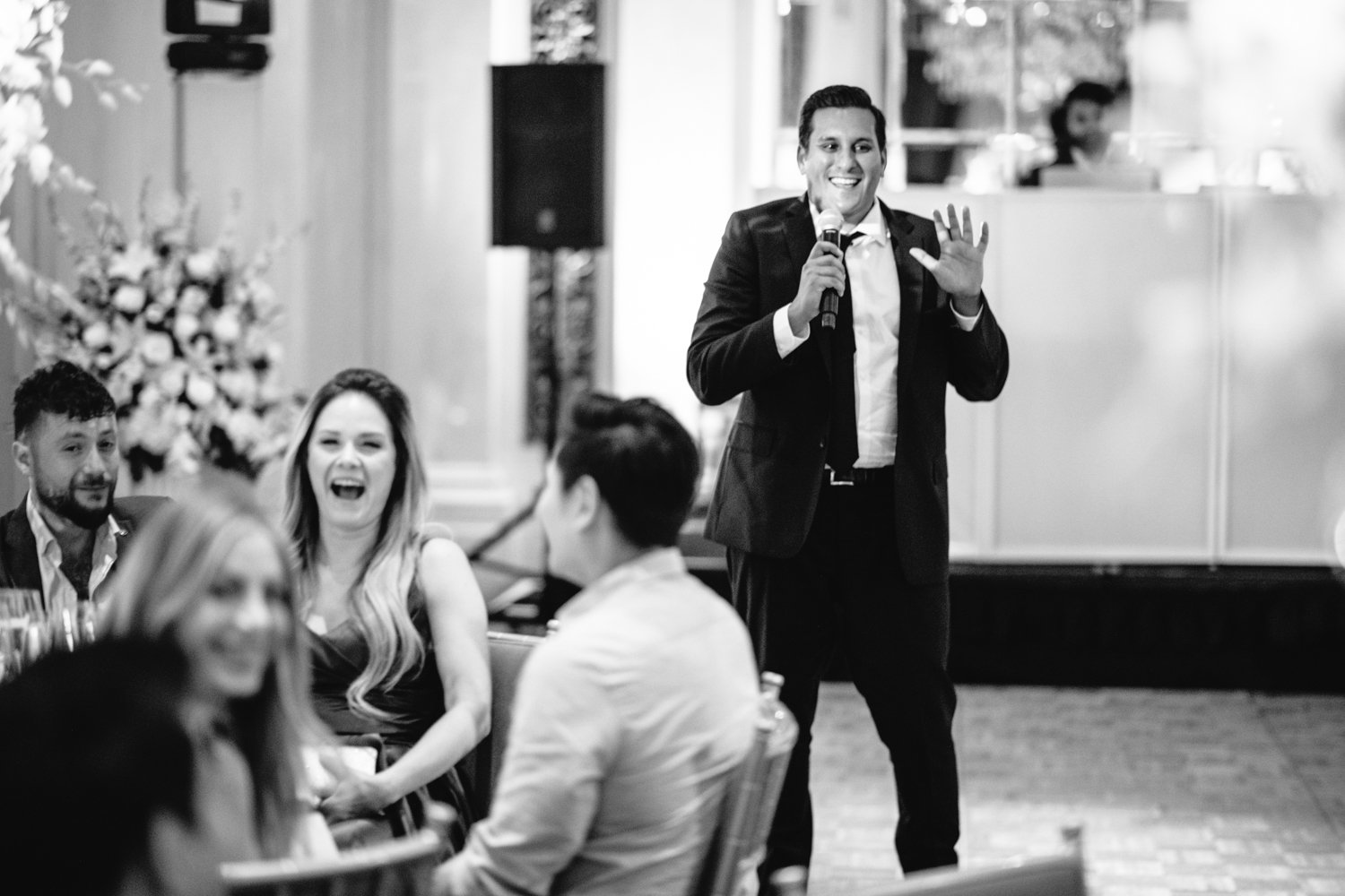Best man is standing and smiling with a microphone in his hand and wedding guests seated at their table in the foreground are smiling and laughing.

Manhattan Luxury Wedding. New York Luxury Wedding Photographer. Wedding in Manhattan. NYC Luxury Wedding.