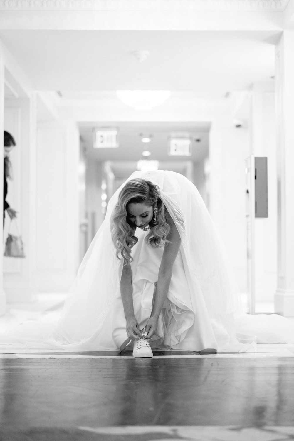 Bride leans over in her wedding dress and ties her white sneaker.

Manhattan Luxury Wedding. New York Luxury Wedding Photographer. Wedding in Manhattan. NYC Luxury Wedding.