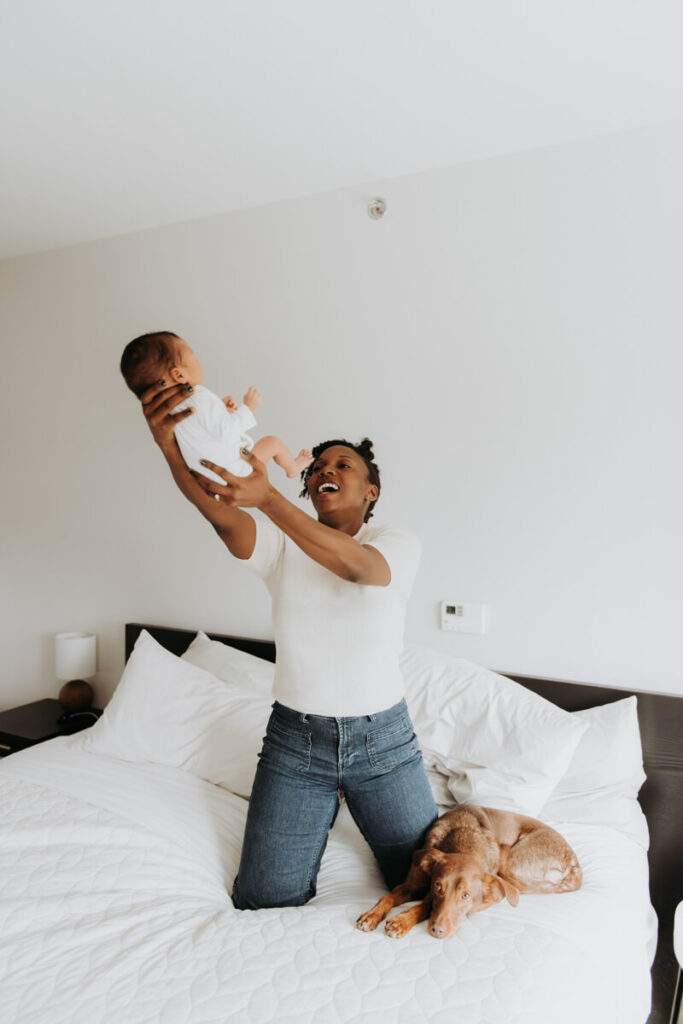 Mother kneels on her bed next to the family dog and holds her newborn baby up in the air.

Newborn Photography. Brooklyn Newborn Portraits. Lifestyle Newborn Photographer. Brooklyn Family Photography.